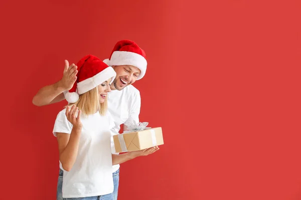 Mąż dając Boże Narodzenie prezent dla żony przed kolorowym tłem — Zdjęcie stockowe