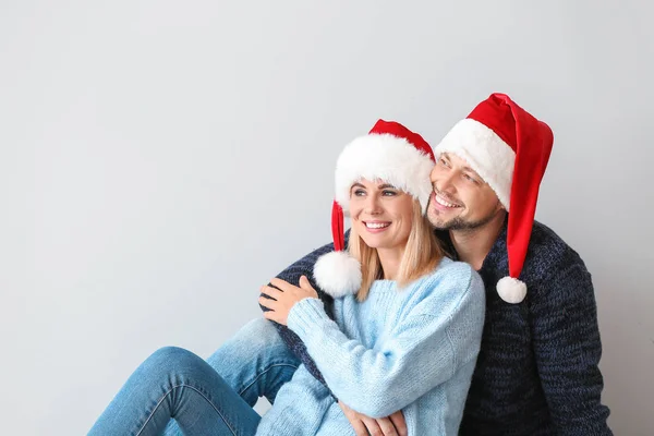 Happy couple in Santa hats on light background — Stock Photo, Image