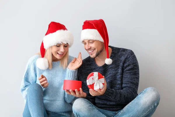 Happy couple in Santa hats and with Christmas gift on light background — Stock Photo, Image