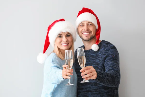 Feliz pareja en los sombreros de Santa beber champán sobre fondo claro — Foto de Stock