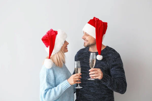 Feliz pareja en los sombreros de Santa beber champán sobre fondo claro — Foto de Stock