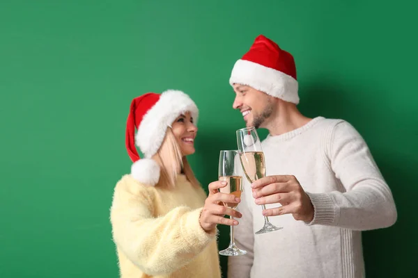 Feliz pareja en los sombreros de Santa beber champán sobre fondo de color — Foto de Stock