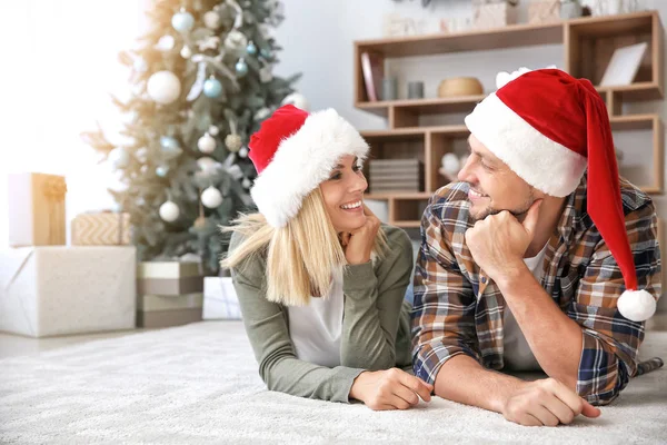 Happy couple in Santa hats at home on Christmas eve — Stock Photo, Image