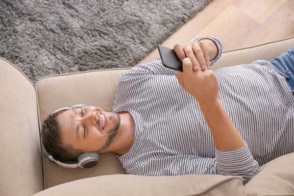 Hombre con teléfono móvil y auriculares relajante en casa —  Fotos de Stock