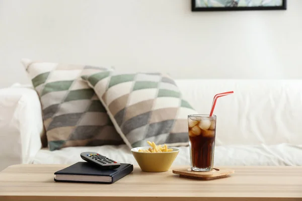 Bicchiere di cola fredda con patatine fritte, libro e telecomando sul tavolo in camera — Foto Stock