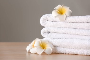 Stack of clean towels with flowers on table against grey background clipart
