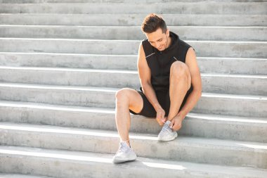 Spor ayakkabı bağcıklarını bağlayan genç bir adam.