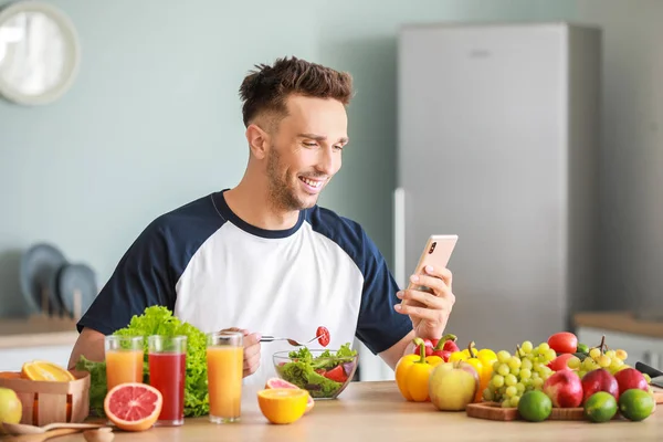 Handsome man counting calories while eating salad in kitchen. Weight loss concept — Stock Photo, Image