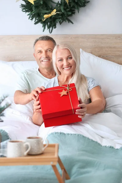 Mature couple with Christmas present in bed at home — Stock Photo, Image