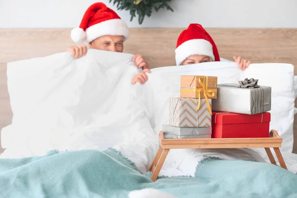 Tray with Christmas gift boxes on bed of mature couple — Stock Photo, Image