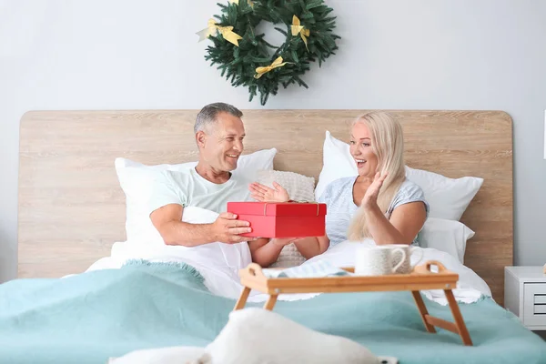 Mogen man som ger sin fru julklapp i sängen hemma — Stockfoto