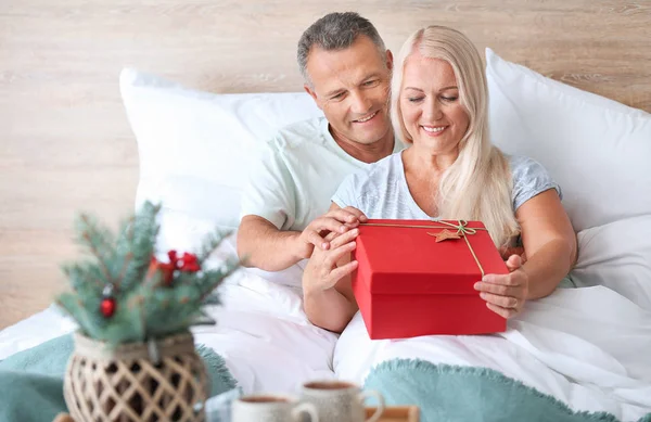 Mature husband giving his wife Christmas present in bed at home — Stock Photo, Image