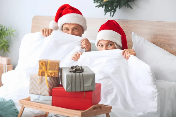 Pareja madura con cajas de regalo de Navidad escondidas detrás de una manta en la cama —  Fotos de Stock