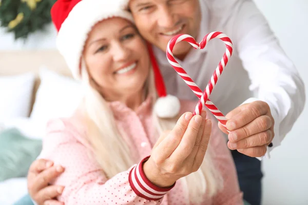 Happy mature couple with Christmas candy canes at home — Stock Photo, Image