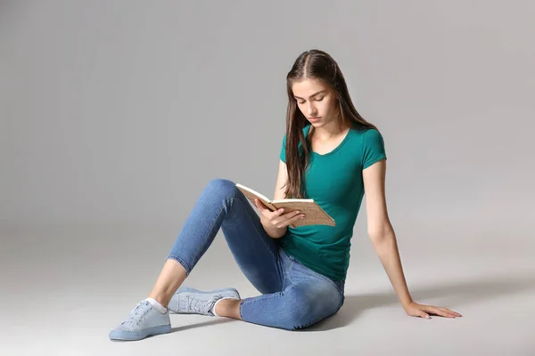 Giovane ragazza con libro su sfondo grigio — Foto Stock