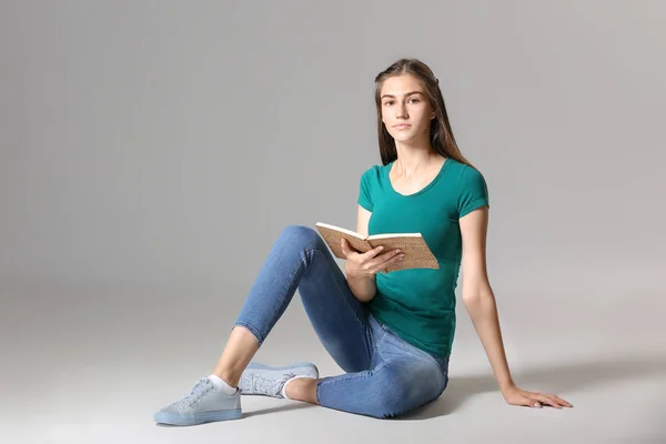 Giovane ragazza con libro su sfondo grigio — Foto Stock