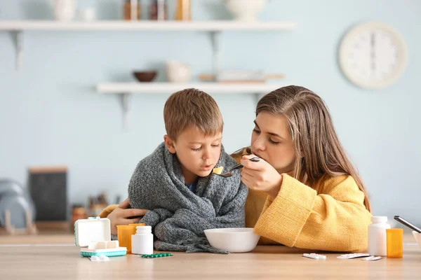 Mother feeding her sick son with chicken soup in kitchen — Stock Photo, Image