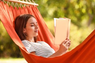 Açık havada hamakta kitap dinlenmiş güzel genç kadın