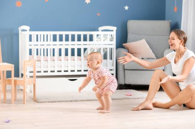 Anne küçük bebeğine evde yürümeyi öğretiyor.