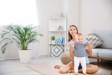 Anne küçük bebeğine evde yürümeyi öğretiyor.