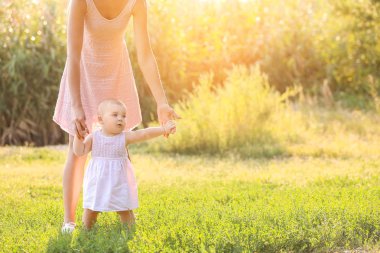 Anne küçük bebeğine dışarıda yürümeyi öğretiyor.
