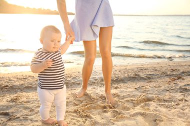 Anne küçük bebeğine nehir kenarında yürümeyi öğretiyor.