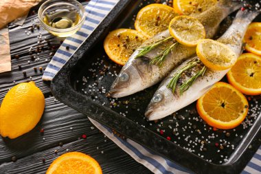 Koyu masa üzerinde taze levrek ve portakal dilimleri ile Tepsi