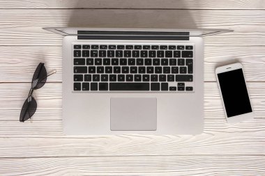 Ahşap arka plan üzerinde cep telefonu ve güneş gözlüğü ile modern dizüstü bilgisayar