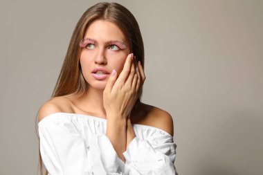 Gri arka planda yaratıcı kirpikleri olan genç kadın