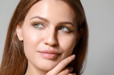 Gri arka planda yaratıcı kirpikleri olan genç kadın