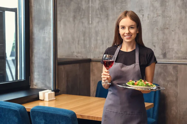 Waitress with glass of wine and dish in restaurant — Stock Photo, Image