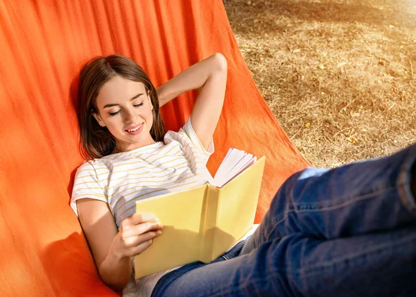 Mooie jonge vrouw met boek rusten in hangmat buitenshuis — Stockfoto