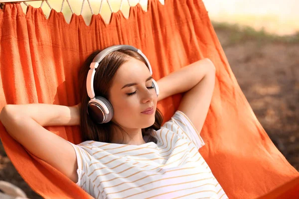 Mooie jonge vrouw met hoofdtelefoon rusten in hangmat buitenshuis — Stockfoto