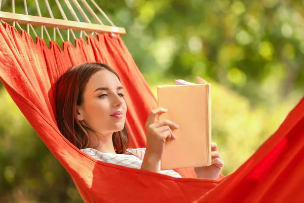 Mooie jonge vrouw met boek rusten in hangmat buitenshuis — Stockfoto