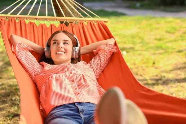 Hermosa mujer joven con auriculares descansando en hamaca al aire libre —  Fotos de Stock