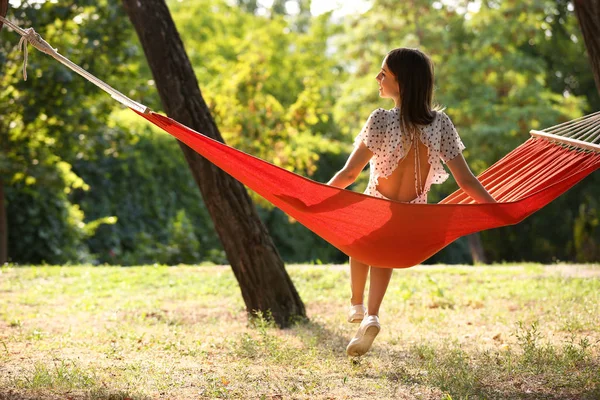 Счастливая молодая женщина сидит в гамаке на открытом воздухе — стоковое фото