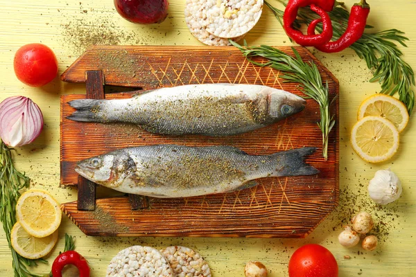 Board with fresh sea bass and ingredients on wooden table — Stock Photo, Image