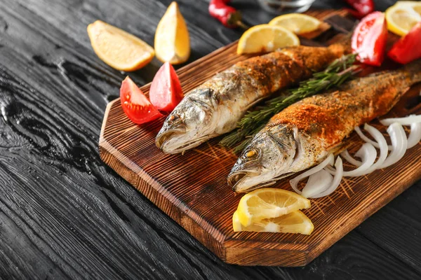 Tablero con sabroso pescado de lubina cocido en mesa oscura —  Fotos de Stock