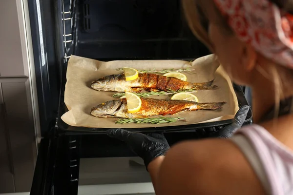 Woman getting out tasty cooked seabass fish of oven in kitchen — Stock Photo, Image