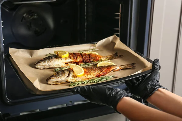 Woman getting out tasty cooked seabass fish of oven in kitchen — Stock Photo, Image