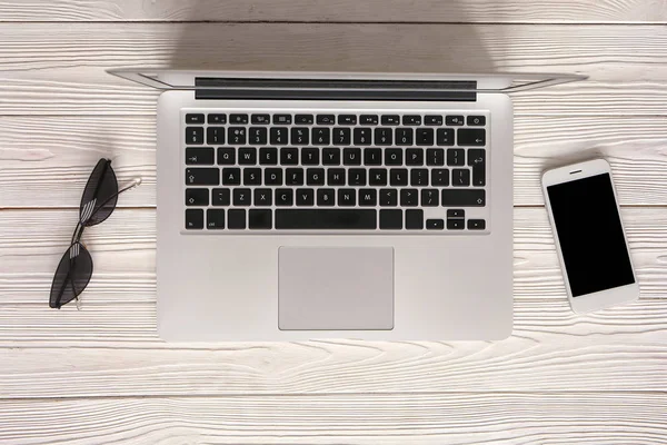 Modern laptop with mobile phone and sunglasses on wooden background — Stock Photo, Image