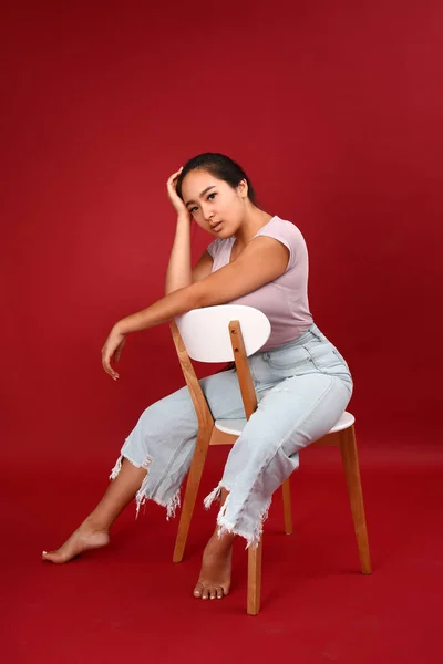 Portrait of beautiful Asian woman sitting on chair against color background