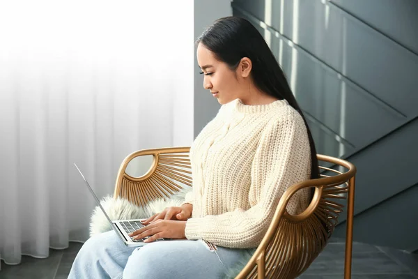 Portrét krásné asijské ženy s laptopem sedícího v křesle doma — Stock fotografie