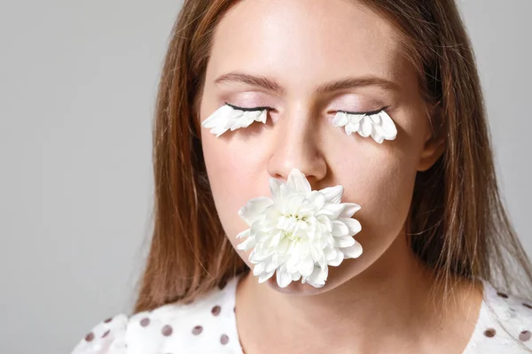 Young woman with creative eyelashes and flower on grey background, closeup