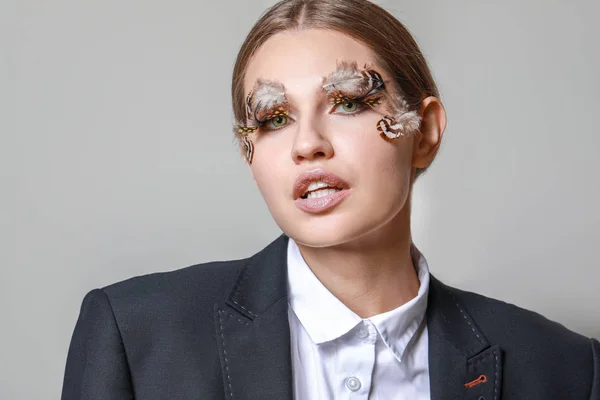 Mujer joven con pestañas y cejas creativas sobre fondo gris — Foto de Stock