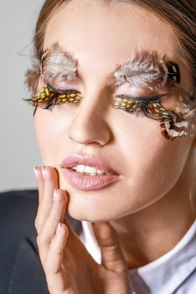 Mujer joven con pestañas y cejas creativas sobre fondo gris, primer plano — Foto de Stock
