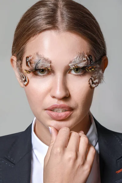 Mujer joven con pestañas y cejas creativas sobre fondo gris —  Fotos de Stock