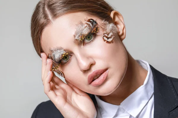 Mujer joven con pestañas y cejas creativas sobre fondo gris — Foto de Stock