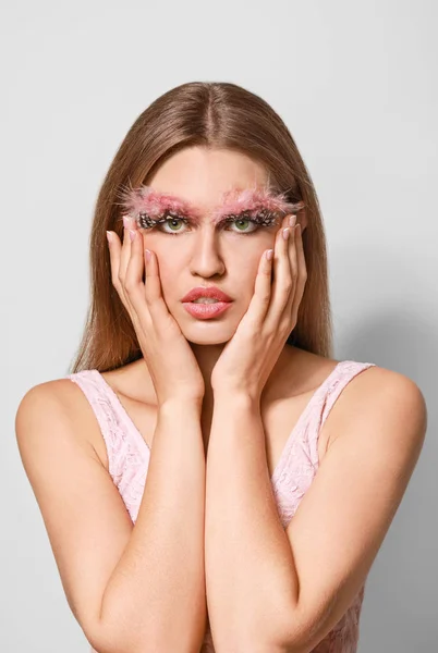 Mujer joven con pestañas y cejas creativas sobre fondo gris — Foto de Stock