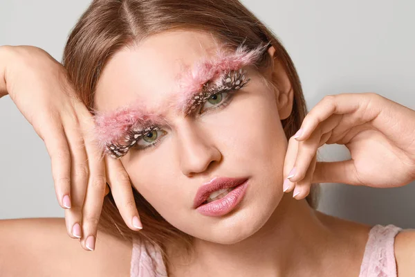 Mujer joven con pestañas y cejas creativas sobre fondo gris — Foto de Stock